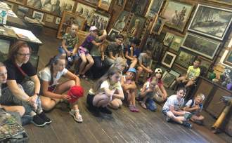 Grupa dzieci siedzących w w Muzeum Jana Wałacha i słuchających prelekcji