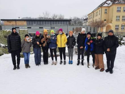 Grupa uczniów z opiekunami na tle szkoły w zimowej scenerii