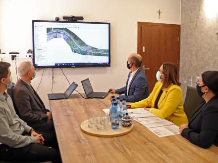 Za stołem siedzą pracownicy i władze gminy Istebna wraz z przedstawicielem firmy Strabag, która zajmie się realizacją II etapu drogi na Zaolziu. Na ścianie wizualizacja remontu drogi.