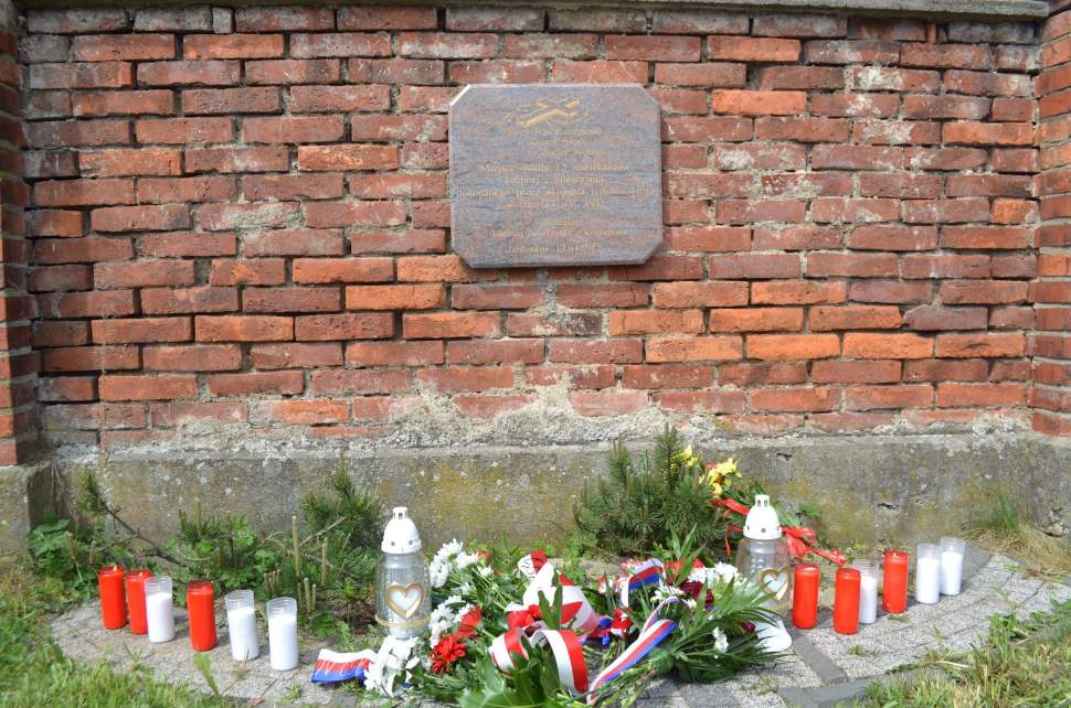 Tablica upamiętniająca mord na mieszkańcach Istebnej i Jaworzynki na murze cmentarza w Jabłonkowie; pod spodem znicze i kwiaty
